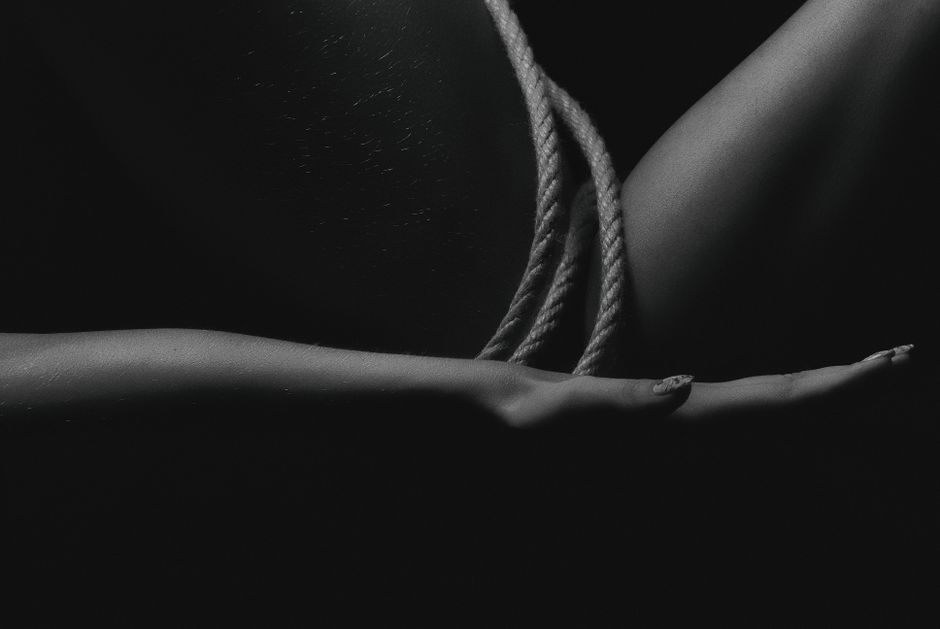 Dark artistic monochrome image featuring close-up of bound hands with rope, emphasizing te