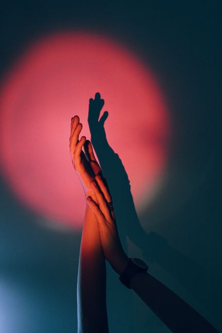 Vertical shot of hands with dramatic shadows under a pink spotlight for creative themes.