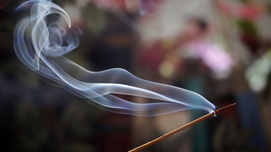 Graceful swirls of incense smoke flow softly against a colorful, blurred background.