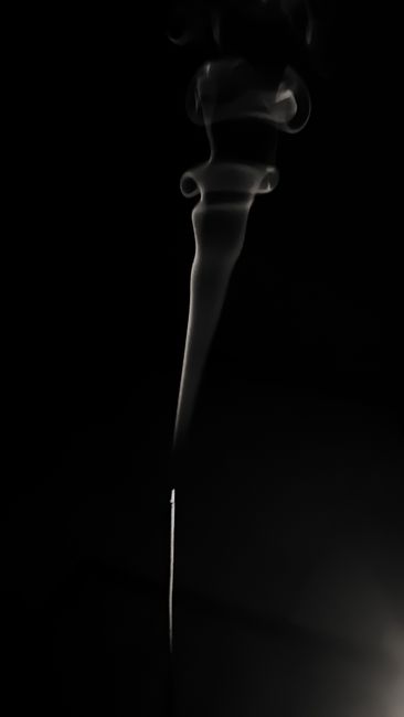 A delicate ribbon of smoke swirls elegantly against a deep black backdrop, creating a calm