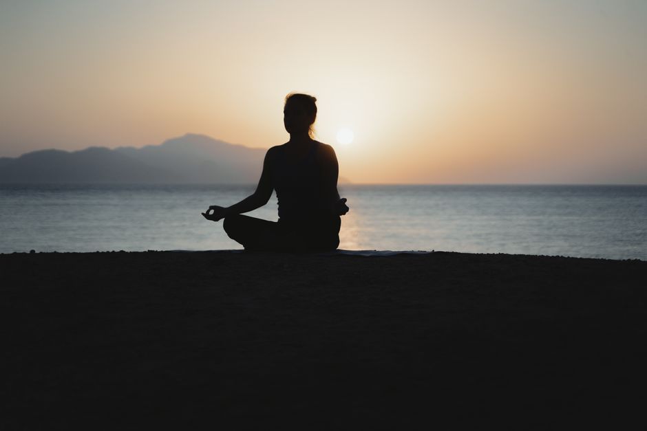 A woman practices meditation with a tranquil ocean sunset backdrop, embodying peace and re