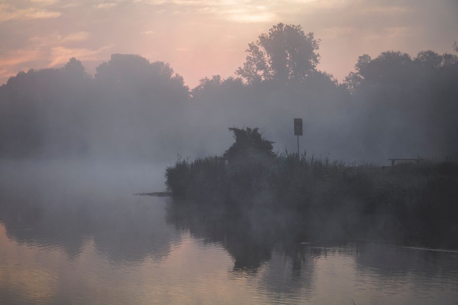 A calming scene of misty sunrise over a peaceful lake surrounded by trees.